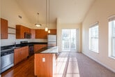 This two-floor residence is defined by its dramatic vaulted ceilings in the main living area, which create an expansive, airy atmosphere that extends through the open-concept kitchen and living room. A ceiling fan is centrally positioned beneath the peak, complementing the generous vertical space. A bank of large windows along one wall floods the interior with natural light, and a sliding glass door provides access to an outdoor balcony.

The kitchen is well-appointed with warm-toned wood cabinetry, dark granite countertops, and a full suite of stainless steel appliances including a gas range, built-in microwave, and refrigerator. A central island with a granite surface provides additional workspace and casual seating. Hardwood flooring grounds the kitchen, transitioning to plush carpet throughout the living area and bedrooms.

The bedrooms are carpeted and bright, each featuring windows with outdoor views. The primary bathroom includes a double-sink vanity with a wood cabinet base, a large mirror, and a walk-in glass-door shower. A secondary full bathroom offers a single vanity and a tub-shower combination with tile surround. Warm neutral tones are consistent throughout, giving the space a cohesive and welcoming character.