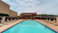 Located in Abilene, this single-floor brick-construction residence is part of a well-established community offering a range of outdoor amenities. The exterior is defined by classic light-toned brick masonry, complemented by a distinctive red entry door that provides a welcoming focal point. Access to the unit is provided via a wooden staircase with a railed landing, offering a semi-private entry experience.

The surrounding grounds are neatly maintained, with concrete walkways connecting the buildings and grassy areas providing a sense of openness between structures. A detached garage with a red door is situated nearby, offering convenient covered parking or additional storage.

A standout feature of the community is the generously sized outdoor swimming pool, enclosed by a combination of wooden and iron fencing for privacy and safety. The pool deck is furnished with multiple lounge chairs, creating an ideal setting for relaxation. An umbrella-shaded seating area adds to the outdoor living appeal. The pool area is directly accessible from the building, making it a practical and attractive amenity for daily use.

The overall ambiance of the property reflects a functional, community-oriented environment with classic Texas architectural character, situated under the open West Texas sky.