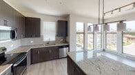 This single-floor residence on Richardson Street in Cayce, South Carolina, presents a thoughtfully designed layout with contemporary finishes and an abundance of natural light. A bright, wide hallway with light wood-style flooring and gold-accented door hardware sets the tone upon entry, leading into the various living spaces.

The open-concept living and dining area is a standout feature, boasting large windows on multiple walls and glass balcony doors that flood the space with natural light and provide outdoor views. A ceiling fan with a light fixture adds functionality, while built-in shelving along one wall offers practical storage. The flooring throughout the main living areas is a light-toned wood-style material that complements the clean, neutral palette.

The kitchen is well-equipped with dark, flat-front cabinetry extending to the ceiling, granite countertops, a tile backsplash, stainless steel appliances including a range, built-in microwave, refrigerator, and dishwasher, and a large island with pendant lighting.

The bedrooms feature plush carpeting, ceiling fans, and windows with outdoor views. Two full bathrooms mirror each other in design, each offering dark wood vanities with granite countertops, a tub-shower combination, and wood-style flooring, creating a cohesive and polished aesthetic throughout.