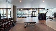 Located in the heart of Hollywood at 1331 N Cahuenga Blvd, this well-appointed fitness center offers a comprehensive workout environment across a single thoughtfully designed floor. The space is divided into distinct training zones, each catering to different aspects of physical fitness.

The main cardio area features a row of treadmills and Concept2 RowERG rowing machines positioned along a floor-to-ceiling glass wall, flooding the space with natural light and offering views of the surrounding neighborhood. Exposed ductwork along the dark ceiling lends an industrial-modern aesthetic, complemented by warm pendant lighting and durable wood-finish flooring throughout.

Adjacent to the cardio zone, a spacious strength training area houses a variety of cable machines and multi-function equipment, supported by round concrete columns that add to the industrial character of the space.

A dedicated free weights room is enclosed by sleek glass barn-style sliding doors, providing a semi-private environment for focused strength training. Inside, floor-to-ceiling mirrors line one wall alongside a full dumbbell rack and a power rack with an adjustable bench, all set on rubber flooring for safety and performance.

Together, these zones create a fully equipped, modern fitness facility designed to support a wide range of training needs in a clean, well-lit, and professionally appointed setting.