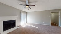 This single-floor residence offers a practical and comfortable layout designed for everyday living. The living room serves as the heart of the home, featuring plush wall-to-wall carpeting, a classic white-mantled fireplace with a tile surround, and a ceiling fan with a built-in light fixture. A sliding glass door floods the space with natural light and opens to an outdoor balcony, offering a seamless indoor-outdoor connection. Neutral gray walls and a textured ceiling carry throughout the home, creating a cohesive and understated aesthetic. The kitchen is efficiently designed with white cabinetry, dark granite-style countertops, wood-look luxury vinyl flooring, and stainless steel appliances including a refrigerator and electric range, along with ample storage including louvered pantry doors. The bedrooms are generously sized, each with soft carpeting, ceiling fans, and natural light provided by window blinds. Closet storage is readily available in the bedroom areas. The bathroom features a clean, all-white tub and shower combination, white cabinetry, a granite-topped vanity with an undermount sink, and wood-look flooring, completing this move-in-ready home with functional style throughout.
