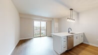 Located at 928 Maple Ave in Downers Grove, IL, this single-floor unit offers a thoughtfully designed open-concept layout with modern finishes throughout. The living area flows seamlessly from the kitchen, featuring wood-style flooring and a sliding glass door that opens to a private balcony with outdoor views of the surrounding neighborhood, including a pool area visible below.

The kitchen is a standout feature, equipped with white shaker cabinetry with matte black hardware, white quartz countertops, a peninsula with an undermount sink and black faucet, and a full suite of stainless steel appliances including a refrigerator, gas range, microwave, and dishwasher. A pendant light fixture adds a contemporary touch above the peninsula.

The bedrooms are carpeted and well-proportioned, with neutral tones and ceiling fans providing a comfortable atmosphere. One bedroom offers direct balcony access through a large sliding glass door, flooding the space with natural light.

The bathroom is finished with wood-look flooring, white shaker vanity cabinetry, a white quartz countertop, and a subway-tiled tub surround. A stacked washer and dryer unit is conveniently located within the bathroom. The overall ambiance is clean, bright, and contemporary.