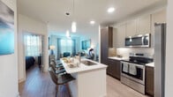 This thoughtfully designed single-floor residence offers a seamless blend of contemporary style and functional living. The open-concept layout connects the kitchen, dining, and living areas into one cohesive space, ideal for both everyday living and entertaining. The kitchen is equipped with stainless steel appliances, including a french door refrigerator, electric range, and built-in microwave. Two-tone cabinetry in white and rich dark wood tones frames crisp white quartz countertops, while a central island with an undermount sink and bar seating serves as the focal point of the space. Pendant lighting adds a refined touch overhead. The living area features wood-look flooring, a ceiling fan, and large windows dressed with sheer curtains and blinds that invite abundant natural light. The bedroom is generously sized, with wide windows offering outdoor views and ample room for a full suite of furniture. The bathroom features a dual-sink vanity with dark wood cabinetry, a wide framed mirror, white quartz countertops, and light tile flooring, lending a clean, spa-like quality. Throughout the residence, a cohesive modern aesthetic is maintained with neutral walls, quality finishes, and consistent design details that create a polished, comfortable atmosphere.