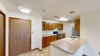 This single-floor unit offers a practical and comfortable layout with a cohesive design characterized by warm oak wood trim, neutral-toned walls, and a mix of tile and plush carpet flooring. The entry foyer welcomes you with tile flooring and immediate access to the kitchen area. The kitchen is well-equipped with warm oak cabinetry, light countertops, a stainless steel refrigerator, an electric range with overhead ventilation, and a peninsula island featuring a built-in sink and pendant lighting — ideal for both cooking and casual dining. The spacious living area extends naturally from the kitchen, offering an open feel with access to natural light through a large window with views of the surrounding area. Two carpeted bedrooms provide comfortable retreats, each featuring built-in closets — one with mirrored sliding doors and another with solid wood panel doors. The unit includes two full bathrooms: one with a tub-shower combination and the other with a glass-enclosed shower stall, both finished with tile flooring and chrome fixtures. A dedicated in-unit laundry room with side-by-side washer and dryer hookups and overhead oak cabinetry adds exceptional convenience to the space.