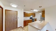 This single-floor unit offers a practical and comfortable layout with a cohesive design characterized by warm oak wood trim, neutral-toned walls, and a mix of tile and plush carpet flooring. The entry foyer welcomes you with tile flooring and immediate access to the kitchen area. The kitchen is well-equipped with warm oak cabinetry, light countertops, a stainless steel refrigerator, an electric range with overhead ventilation, and a peninsula island featuring a built-in sink and pendant lighting — ideal for both cooking and casual dining. The spacious living area extends naturally from the kitchen, offering an open feel with access to natural light through a large window with views of the surrounding area. Two carpeted bedrooms provide comfortable retreats, each featuring built-in closets — one with mirrored sliding doors and another with solid wood panel doors. The unit includes two full bathrooms: one with a tub-shower combination and the other with a glass-enclosed shower stall, both finished with tile flooring and chrome fixtures. A dedicated in-unit laundry room with side-by-side washer and dryer hookups and overhead oak cabinetry adds exceptional convenience to the space.