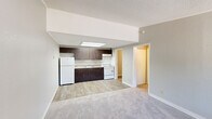 Located in Jupiter, FL, this one-bedroom, one-bathroom unit offers a functional and efficient single-floor layout. The open-concept kitchen and living area serves as the heart of the home, featuring wood-look tile flooring that transitions seamlessly to plush carpeting in the living space. The kitchen is equipped with dark espresso cabinetry, a white refrigerator, electric range, and a sink, all illuminated by a skylight overhead that brings in natural light. Crown molding and a textured ceiling add a subtle architectural detail throughout.

The bedroom is a comfortable, carpeted retreat featuring a ceiling fan with light fixture, a window with blinds offering natural light and outdoor views, and access to closet space. Three closets total are distributed throughout the unit, providing generous storage. A hallway connects the main living areas to the bedroom and bathroom, which features dark wood cabinetry with a white countertop vanity, a toilet, and a shower-tub combination with a curtain rod.

A dedicated utility room houses the water heater and additional mechanicals. Neutral gray walls, consistent trim work, and wood-look flooring in the entry area round out this well-organized and practical unit in Jupiter, Florida.