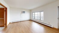This 2-bedroom, 2-bathroom residence in Monona, Wisconsin offers a thoughtfully arranged single-floor layout with a clean, neutral aesthetic throughout. The living room is a bright, open space featuring light wood-style flooring, a wall-mounted air conditioning unit, and a large picture window with decorative glass detailing that frames expansive water views, filling the room with natural light. A ceiling fan and half-wall partition with a wood-topped ledge define the transition into the dining area, which also enjoys hardwood-style flooring and an additional window. The galley-style kitchen is efficiently designed with ample white cabinetry extending to the ceiling on both sides, light countertops, a double-basin sink, and white appliances including a refrigerator and range. Both bedrooms are carpeted and feature individual windows — the primary bedroom enjoys a pleasant outdoor view of green landscaping, while the second bedroom offers a view of the surrounding neighborhood. The two bathrooms are clean and functional, one featuring wood-toned cabinetry, a single-basin vanity, overhead storage cabinets, and a tiled shower area with baseboard heating. Baseboard heating is present throughout the unit, ensuring year-round comfort in the Wisconsin climate.