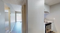 This single-story unit offers a thoughtfully arranged floor plan across two bedrooms and one bathroom. The kitchen is a functional galley-style space featuring white cabinetry with contemporary hardware, granite-look countertops, and stainless steel appliances including an electric range and refrigerator. A skylight overhead floods the kitchen with natural light, enhancing the clean, bright aesthetic. Light-toned hardwood-style flooring runs throughout, adding a cohesive and modern feel underfoot. Textured walls and a popcorn ceiling lend a classic character to the interiors. A hallway connects the main living areas, leading toward a room that benefits from natural light through vertical blinds-covered windows, offering a view of the outdoors. The overall ambiance is clean and move-in ready, with updated finishes that balance practicality and comfort. The layout makes efficient use of its footprint, providing dedicated spaces for cooking, living, and sleeping within a compact but well-organized design.