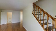 Located at 554 Connecticut Avenue in Norwalk, Connecticut, this two-story residence offers a clean, well-maintained interior with a welcoming and functional layout. The main level is characterized by warm hardwood flooring that extends throughout the open living areas, complemented by crisp white walls and bright, neutral tones that create an airy and inviting atmosphere. A classic wooden staircase with turned spindle balusters and a sturdy handrail serves as a focal point of the main level, providing an elegant transition between the two floors. The staircase detailing adds a touch of traditional craftsmanship to the otherwise understated interior. Baseboard heating units are positioned along the walls, ensuring comfortable climate control throughout the colder months. The open sightlines between rooms on the main floor promote a sense of connectivity and spaciousness, with natural light filtering through to illuminate the interior. The neutral color palette and hardwood flooring provide a versatile backdrop suitable for a variety of furnishing styles. Overall, the space presents a tidy, move-in ready environment with practical finishes and timeless architectural details that make it a solid and comfortable residence in the Norwalk, CT area.