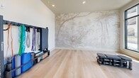 Located at 201 Hills Rd in Panama City Beach, FL, this comprehensive fitness facility spans a generously sized single floor, offering a diverse range of workout zones designed to accommodate all levels of training. The space is defined by its clean, modern aesthetic, featuring light hardwood flooring in the strength and studio areas, durable rubber flooring in the functional training zones, crisp white walls, and recessed lighting throughout.

The main cardio area lines an entire wall of floor-to-ceiling windows, flooding the space with natural light and providing views of the surrounding outdoors. Treadmills, ellipticals, rowing machines, and air bikes are thoughtfully arranged to take full advantage of this bright, airy environment, with ceiling fans adding to the comfort overhead.

A dedicated strength training section features cable machines, dumbbell racks, and weight benches spread across light hardwood floors. The functional training zone is equipped with heavy bags, TRX suspension systems, battle ropes, medicine balls, and a pull-up rig. A separate studio room offers a serene retreat, distinguished by a striking nature-inspired mural wallcovering, light wood flooring, and yoga and stretching accessories. An additional bright studio room features large windows and an elegant pendant light fixture, making it ideal for Pilates or personal training sessions.