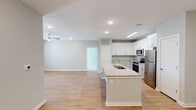 This single-floor residence in Huntsville, Alabama offers a thoughtfully designed open-concept layout that seamlessly connects the kitchen, dining, and living areas. The kitchen is a standout feature, equipped with crisp white cabinetry, granite countertops, and a full suite of stainless steel appliances including a range, microwave, and refrigerator. A central island with an undermount sink and granite surface provides additional prep space and serves as a natural gathering point. Light wood-look flooring flows throughout the main living areas, complementing the soft sage-green walls and white trim. The living area benefits from recessed lighting and a ceiling fan, with a glass door leading to an outdoor area that brings in natural light. The bedrooms are carpeted for comfort and each feature ceiling fans and ample natural light through slatted windows. The bathrooms are finished with granite-topped vanities, tile flooring, and a walk-in shower enclosed by sliding glass doors in the primary bath. A dedicated laundry area with a washer and dryer is conveniently accessible off the kitchen. Clean lines, neutral tones, and modern finishes throughout give this residence a fresh, move-in-ready appeal.