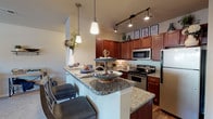 This single-story, 2-bedroom, 2-bathroom residence offers a thoughtfully designed layout with quality finishes throughout. The kitchen serves as a central highlight, showcasing rich cherry wood cabinetry extending to the ceiling, granite countertops, and a full suite of stainless steel appliances including a range, microwave, and refrigerator. A peninsula with pendant lighting provides additional prep space and casual seating, complemented by track lighting and wood-look flooring that adds warmth to the space.

The living area features large windows with views of the surrounding neighborhood, allowing natural light to fill the room and creating an inviting atmosphere. Both bedrooms are generously proportioned, each equipped with ceiling fans and walk-in closets featuring wire shelving systems. The carpeted bedrooms provide a comfortable, quiet retreat.

Each bathroom is appointed with granite-topped vanities and dark wood cabinetry, maintaining the consistent design language found throughout the home. A dedicated in-unit laundry room accommodates a full-size washer and dryer side by side, adding everyday convenience. The overall design balances functional living spaces with cohesive, quality finishes.