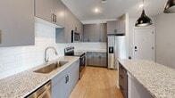 Located at 5306 Acadia Heights Dr in Charlotte, NC, this thoughtfully designed one-bedroom, one-bathroom residence offers a clean, modern aesthetic across a single floor. The open-concept layout seamlessly connects the living area to the kitchen, maximizing the efficient use of space while maintaining an airy, welcoming feel.

The kitchen is a standout feature, showcasing sleek gray cabinetry, granite countertops, a white subway tile backsplash, and a full suite of stainless steel appliances. A central island with a white base and granite top provides additional prep space and a natural focal point, accented by two matte black pendant lights overhead. Light wood-style flooring runs throughout the main living areas, adding warmth and continuity.

The living area opens to a private balcony, allowing natural light to fill the space and offering outdoor views. The bedroom is carpeted for comfort, features a ceiling fan with light fixture, and includes a window for natural light. A walk-in closet with wire shelving provides ample storage.

The bathroom is finished with clean, white subway tile in a glass-door walk-in shower, complemented by neutral-toned walls and wood-style flooring. The overall design palette of soft grays, whites, and warm wood tones creates a cohesive and contemporary living environment.