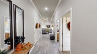 This single-story 2-bedroom, 2-bathroom home combines practical design with warm, inviting character throughout. A wide central hallway with wood-look flooring and crown molding connects all rooms, setting an elegant tone from the moment you enter. The living room features elevated ceilings with crown molding detail, a ceiling fan, recessed lighting, and natural light from windows overlooking greenery outside. The kitchen showcases natural wood cabinetry reaching toward the ceiling, black appliances, recessed lighting, and a window above the sink that fills the space with daylight. Adjacent to the kitchen, the dining area accommodates a full dining set beneath a classic chandelier, with a sliding glass door providing additional natural light and outdoor access. The primary bedroom offers a generous footprint with a distinctive tray ceiling, adding architectural depth and a sense of height. The second bedroom is cozy and comfortable with ample closet access. Both bathrooms are well-finished; one features a walk-in tiled shower with mosaic accent detail and warm wood vanity cabinetry. The dedicated laundry room houses a full-size washer and dryer. Throughout the home, wood-look hard flooring and a neutral gray-and-white palette create a cohesive, modern aesthetic.