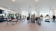 Located at 425 W Trade St in the heart of Charlotte, NC, this modern fitness center offers a comprehensive, multi-zone layout designed to support a wide range of workout routines. The facility is bathed in natural light through floor-to-ceiling windows that frame views of the surrounding Charlotte skyline, creating an energizing atmosphere throughout.

The main strength training area features a robust selection of resistance machines, free weights, weight benches, and a cable station, all arranged on durable carpet-tile flooring. Full-length mirrors line the walls, enhancing the sense of space and aiding in proper form. A dedicated cardio room provides an array of treadmills, upright and recumbent bikes, and elliptical trainers positioned directly in front of expansive windows. A vibrant, textured exposed brick accent wall with colorful artistic detailing adds character to this zone, complemented by a wall-mounted flat-screen TV and ceiling fans overhead.

A separate studio space features rich hardwood flooring, recessed lighting, ceiling fans, and a mounted flat-screen TV, making it well-suited for yoga, stretching, or group fitness classes. Interior glass walls connect this studio to the broader facility. The entry area includes posted fitness rules and a clean, open transition space. The facility's crisp white walls, consistent modern finishes, and thoughtful zoning make it a well-appointed amenity space.