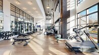 Located at 652 Angier Ave NE in Atlanta's vibrant Old Fourth Ward neighborhood, this state-of-the-art fitness facility delivers an impressive workout environment defined by its striking industrial-modern design. Soaring double-height ceilings with exposed ductwork and pendant lighting create an open, energizing atmosphere throughout the single-floor space. Warm hardwood flooring runs the length of the facility, contrasting beautifully with the raw texture of exposed dark brick columns and crisp white walls. Expansive floor-to-ceiling steel-framed windows flood the interior with abundant natural light while offering views of the surrounding greenery, making cardio sessions feel connected to the outdoors. The main floor is thoughtfully organized into distinct training zones. A dedicated cardio section houses a row of treadmills and elliptical machines positioned directly in front of large windows, alongside rowing machines and Assault-brand fitness equipment. The strength training area features a full rack of dumbbells, adjustable benches, cable machines, and a functional training rig complete with battle ropes, medicine balls, and resistance bands. A separate spin studio with Peloton bikes offers a focused cycling experience bathed in natural light. Full-length mirrors amplify the sense of space and support proper form throughout. This facility combines premium equipment, architectural character, and an abundance of natural light into a cohesive and motivating training environment.