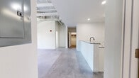 This contemporary 3-bedroom, 2-bathroom unit offers a well-designed single-floor layout with a clean, modern aesthetic defined by polished concrete floors and crisp white walls throughout. The open-concept kitchen serves as a central feature, equipped with white shaker cabinetry, granite countertops, a subway tile backsplash, stainless steel appliances including a refrigerator and microwave, and a peninsula with a matte black faucet that flows into the main living area. The living space is bright and open, with exposed overhead infrastructure in one section adding an industrial character. The spacious primary bedroom benefits from its own wall-mounted mini-split HVAC unit and a double-door closet, while another bedroom features a floor-to-ceiling window that frames outdoor views and fills the room with natural light. A walk-in closet with wood hanging rods provides generous storage. The two bathrooms are finished with small-format tile flooring in a classic grid pattern and matte black fixtures. One bathroom includes a tiled tub-shower combination with a granite vanity, while the other features a stand-alone tiled shower stall. The overall ambiance is clean, minimal, and move-in ready, with modern finishes that lend a cohesive, contemporary feel to every room.
