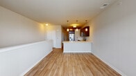 This single-floor residence in Romeoville, Illinois, offers a thoughtfully designed open-concept layout that seamlessly connects the living area and kitchen. The main living space is finished with warm, light-toned hardwood-style flooring that extends throughout, contributing to a bright and cohesive atmosphere. A clean white half-wall borders the living area, defining the space without interrupting the open sightlines toward the kitchen.

The kitchen is a standout feature, equipped with rich dark espresso cabinetry, stainless steel appliances including a refrigerator with ice and water dispenser, an electric range, and a built-in microwave. A peninsula with a light-toned countertop and an integrated sink provides additional prep and seating space. Stylish pendant lights hang above the peninsula, adding both task lighting and a modern aesthetic touch.

A dedicated laundry area houses a stacked washer and dryer unit behind a closet door, offering practical convenience within the unit. The carpeted area near the laundry provides a softer transition into the more private areas of the home.

The bathroom is finished with light hardwood-style flooring, a dark vanity with a white countertop, a walk-in glass-enclosed shower, and clean white walls that create a fresh, functional space.