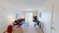 This single-floor residence offers a thoughtfully arranged layout across several well-defined spaces. The living room serves as the heart of the home, featuring plush wall-to-wall carpeting, neutral walls, and a large sliding glass door flanked by vertical blinds that frames outdoor views of natural wooded scenery while flooding the room with natural light. Framed artwork accents the walls, adding character to the bright, open atmosphere.

The galley-style kitchen is efficiently designed with dark wood cabinetry lining both walls, granite-toned countertops, wood-look flooring, and white appliances including a gas range and refrigerator, providing ample storage and workspace.

The primary bedroom is a comfortable retreat with carpeted flooring, a ceiling fan with light fixture, and a window with blinds offering soft natural light. A second bedroom mirrors this layout with its own window and cozy proportions.

The bathroom features a shower/tub combination with a decorative curtain and neutral finishes, completing the unit's functional design. Throughout, the residence maintains a clean, understated aesthetic with consistent neutral tones and practical finishes.