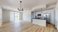 This single-floor residence showcases a clean, modern design with a thoughtfully arranged open-concept layout. The combined living and dining area is anchored by light-toned hardwood-style flooring that extends throughout the main living spaces, complemented by a striking black metal chandelier. Large sliding doors and multiple windows allow natural light to fill the space, enhancing the bright, airy ambiance created by the white walls and neutral palette.

The kitchen is well-appointed with white shaker-style cabinetry, bold dark countertops, a subway tile backsplash, and a full suite of stainless steel appliances including a refrigerator with ice maker, electric range with microwave, and dishwasher. A peninsula with an undermount sink and pendant lighting above provides additional workspace and serves as a natural divider between the kitchen and living area.

The bedrooms feature plush carpeting and tray ceilings with ceiling fans, offering a comfortable and relaxed atmosphere. Natural light enters through blinded windows, adding warmth to each room. The bathroom includes wood-look tile flooring, a dark-toned vanity with gold hardware, a framed medicine cabinet mirror, and a tub-shower combination, completing the space with practical yet stylish finishes.