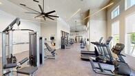 Located at 3065 Champion Ring Rd in Fort Myers, Florida, this expansive fitness center offers a comprehensive, professionally equipped exercise facility spread across a single open floor. The space is designed with soaring ceilings that create an open, airy atmosphere, while large clerestory windows along the upper walls flood the interior with natural light and offer views of the surrounding outdoor greenery and pool area.

The main exercise floor is finished with durable stone-look tile and hosts an extensive selection of Matrix-brand strength and cardio equipment, including cable machines, multi-functional weight stations, dumbbell racks, treadmills, ellipticals, and a stair climber. Full-length mirrors are strategically placed throughout to enhance the sense of space and assist with form during workouts. Overhead, large modern ceiling fans and sleek linear LED lighting fixtures maintain comfort and visibility throughout.

A dedicated spin studio is separated from the main floor by glass-paneled partition doors. This room features light hardwood flooring, a full mirrored wall, wall-mounted flat-screen TVs, and a row of Matrix cycling bikes, making it ideal for group fitness sessions. Additional functional training equipment, including TRX suspension systems, battle ropes, kettlebells, and a power rack, rounds out the facility's offerings, providing options for a wide variety of training styles.