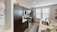 This single-story residence offers a thoughtfully designed layout that balances functionality with contemporary style. The kitchen is a standout feature, equipped with stainless steel appliances including a range, microwave, and refrigerator, complemented by dark espresso cabinetry, light quartz countertops, and a mosaic tile backsplash. Wood-look flooring runs throughout the main living areas, adding warmth and continuity.

The living room is bright and welcoming, with multiple windows dressed in white blinds and gold curtain panels that invite natural light. A ceiling fan overhead adds comfort, while the open layout connects seamlessly to a dedicated dining area, which features its own large window and wall-mounted display shelving.

The bedrooms are distinctly styled, each featuring deep-toned accent walls in navy and teal, creating a cozy and visually striking atmosphere. The primary suite connects to a well-appointed bathroom with dark vanity cabinetry, a large mirror, and direct access to a walk-in closet with built-in shelving and hanging rods. A second bathroom mirrors this refined aesthetic with similar finishes and geometric wall décor, reinforcing the cohesive modern design found throughout the space.