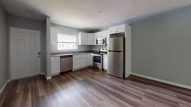 Cocina moderna con elegantes electrodomésticos de acero inoxidable, elegantes gabinetes blancos y cálidos pisos de madera, que ofrece un espacio de cocina acogedor y funcional. - Sunny Creek Apartments
