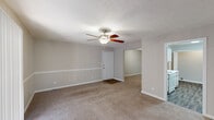 Located in Hattiesburg, MS, this single-floor, 1-bedroom, 1-bathroom residence offers a practical and comfortable layout designed for efficient living. The living area is generously sized, featuring soft wall-to-wall carpeting, neutral gray walls with a chair rail detail, a textured ceiling, and a ceiling fan with light fixture. A sliding glass door with vertical blinds provides direct access to a private outdoor deck and fills the space with natural light. A second view of the living area reveals a front entry door and an open sightline into the bedroom, creating a connected and easy-to-navigate floor plan. The kitchen is equipped with light wood cabinetry, ample upper and lower storage, a double-basin stainless steel sink, white countertops, and a full-size refrigerator, alongside wood-look flooring for easy maintenance. The bedroom is a well-proportioned, carpeted room with its own ceiling fan and a large sliding door that allows additional natural light. A spacious walk-in closet with wire shelving provides generous storage. The bathroom features a full soaking tub and shower combination with chrome fixtures and wood-look flooring, completing this well-rounded residence.