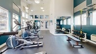 Located at 12312 Sherman Way in Los Angeles, CA, this fitness center offers a well-appointed, single-floor layout designed to support a comprehensive workout experience. The space is composed of a main gym area, a bathroom, and a dedicated entrance.

The gym is the centerpiece of this facility, immediately impressing with its soaring vaulted ceilings and bold teal accent walls that create a dynamic, energizing atmosphere. Rows of large windows flood the space with natural light, enhancing the open and airy feel. Pendant lighting fixtures hang from the high ceiling, providing additional illumination throughout the workout area. The gym is equipped with a wide range of cardio machines — including ellipticals, stationary bikes, and treadmills — as well as a multi-station cable machine and a dedicated free weights section with a dumbbell rack and weight bench. Floor-to-ceiling mirrors in the free weights area expand the sense of space and aid in form correction. A wall-mounted television adds to the facility's amenities.

The bathroom is finished with neutral tile wainscoting and light ceramic tile flooring, and includes ADA-compliant fixtures such as grab bars and accessible sink and toilet installations, along with a urinal — making it a functional, inclusive space.

The entrance provides a clean, welcoming transition into the facility.