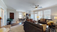 This thoughtfully designed single-floor residence offers a seamless open-concept layout connecting the living, dining, and kitchen areas. The living room is a welcoming focal point, anchored by a fireplace and outfitted with crown molding, a ceiling fan, and large windows that allow generous natural light to fill the space. A glass door provides direct access to a private balcony, offering outdoor views. The dining area accommodates a round table for four and features a door with transom window that also opens to the exterior, enhancing the flow of light throughout. The kitchen is equipped with dark espresso cabinetry, granite countertops, a subway tile backsplash, stainless steel appliances, and a window above the sink for additional natural light. The residence includes two well-sized bedrooms, each fitted with plush carpeting, large windows with outdoor views, and ceiling fans for comfort. The full bathroom features hardwood-style flooring, a dark vanity with granite countertops, and a full tub-shower combination. Throughout the home, hardwood-style flooring in the main living areas contrasts with soft carpet in the bedrooms, creating a warm and cohesive aesthetic.
