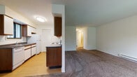 This single-floor residence offers a well-organized and functional layout designed for comfortable everyday living. The galley-style kitchen is efficiently arranged with white cabinetry featuring wood-tone trim, dark laminate countertops, hardwood-style flooring, and a full suite of white appliances including a refrigerator, dishwasher, and electric range. A louvered bi-fold door provides access to a closet within the kitchen area, adding convenient storage. The open living area flows seamlessly from the kitchen, featuring plush wall-to-wall carpeting and neutral walls that create a calm, versatile backdrop. A sliding glass door in the living room opens to a private balcony, offering pleasant outdoor views of surrounding greenery. A wall-mounted air conditioning unit and baseboard heating ensure year-round comfort throughout the space. The bedroom is generously proportioned, finished with the same warm carpeting, and includes a dedicated closet area. A hallway connects the main living spaces to the bedroom and bathroom. The bathroom features light tile flooring, a white vanity with an overhead mirror, and a louvered bi-fold closet door. Overall, the space presents a clean, practical, and well-appointed interior suited for a variety of living arrangements.