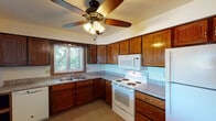 Located at 1102 Logan St in Marquette, Michigan, this single-floor unit offers a practical and comfortable layout designed for everyday living. The kitchen is a standout feature, outfitted with rich oak cabinetry, granite-look countertops, and white appliances including an electric range, over-the-range microwave, and dishwasher. A ceiling fan with light fixture provides ventilation and ambiance, while a window above the sink fills the space with natural light and views of surrounding greenery. The kitchen connects to the living area via a convenient pass-through opening, creating an open and communicative flow between spaces. The living room is generously proportioned, featuring soft carpeting, neutral walls, and a textured ceiling. A wood-trimmed window frames outdoor views, and baseboard heating units run along the walls to ensure warmth during Michigan's cold seasons. An additional carpeted room, likely a bedroom, also features a window with an exterior view and baseboard heating. The full bathroom is clean and functional, appointed with tile flooring in warm tones, a tub-shower combination with a white surround, and a vanity with a white countertop. Throughout the unit, the design prioritizes functionality and comfort, making it a solid and well-maintained space in the Marquette area.