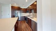 This single-floor residence offers a thoughtfully designed layout that balances modern finishes with functional living spaces. The kitchen is a standout feature, showcasing rich dark-stained cabinetry with sleek bar-pull hardware, crisp light quartz countertops, and a striking mosaic tile backsplash in neutral tones. A full suite of stainless steel appliances — including a gas range, built-in microwave, dishwasher, and a French door refrigerator with an in-door ice and water dispenser — rounds out this well-appointed cooking space. A kitchen island provides additional counter space and separates the kitchen from the main living area. The open living area is bathed in natural light through large windows and a sliding glass door that leads to a private balcony with exterior views of the surrounding community. Warm-toned hardwood flooring runs throughout the kitchen and living spaces, adding continuity and warmth. The bedroom is a comfortable, well-lit room with soft carpeting and dual windows that invite in natural daylight. The bathroom is finished cleanly with a soaking tub and shower combination framed by white subway tile walls, complemented by brushed nickel fixtures for a polished, contemporary look throughout.
