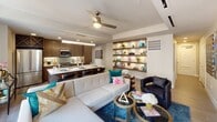 This well-appointed single-floor residence showcases a thoughtfully designed open-concept layout that seamlessly connects the main living spaces. The kitchen is a functional centerpiece, featuring sleek walnut-toned cabinetry, quartz countertops, stainless steel appliances including a range, built-in microwave, and refrigerator, along with a generous island that doubles as a breakfast bar. Pendant and recessed lighting illuminate the space effectively.

The adjoining living area is warm and inviting, highlighted by a ceiling fan, built-in display shelving with integrated lighting, and ample room for comfortable seating arrangements. The open flow between kitchen and living creates an ideal environment for entertaining.

The bedroom is a tranquil retreat, distinguished by a soft teal accent wall, light wood-look flooring, a ceiling fan, and dual windows offering urban city views. A row of gold-framed mirrors above the bed adds an elegant decorative touch.

The bathrooms are finished to a high standard, featuring walnut cabinetry, quartz vanity surfaces, LED-backlit mirrors, and a glass-enclosed shower. Dual vanity areas provide generous storage and functionality, completing this refined and contemporary residence.