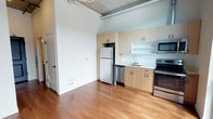 Located at 624 Yale Ave N in Seattle's South Lake Union neighborhood, Unit 826 is a thoughtfully designed single-floor residence that blends modern finishes with industrial character. The open-concept layout creates a seamless flow between the living and kitchen areas, maximizing the sense of space throughout. The kitchen is well-appointed with light wood cabinetry, stainless steel appliances including a refrigerator, dishwasher, and electric range, as well as a microwave and a clean, minimalist countertop workspace. An open shelf adds a contemporary touch to the kitchen design. Warm-toned hardwood flooring runs throughout the main living area, adding a welcoming contrast to the crisp white walls. The exposed concrete ceiling and visible industrial ductwork lend the space an urban loft aesthetic, highlighting the building's architectural character. Natural light fills the space, enhancing the open and airy feel. The unit also features floor-level venting and clean wall finishes, reflecting a practical yet stylish approach to urban living. Situated in one of Seattle's most vibrant and walkable neighborhoods, this residence offers an ideal blend of modern comfort and city convenience.