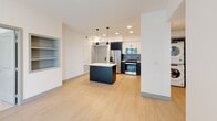 This well-appointed single-floor residence offers a thoughtfully designed layout with contemporary finishes throughout. The open-concept kitchen serves as a focal point, showcasing two-tone cabinetry in white and charcoal with black hardware, a striking geometric tile backsplash, stainless steel appliances, and a large central island with a clean white countertop. Pendant lighting above the island adds a modern industrial touch, while light wood-style flooring extends through the living and kitchen areas, enhancing the sense of openness.

The living area is bright and airy, benefiting from natural light and direct access to a private outdoor balcony through a glass-paned door. Ceiling fans are present in both the living space and bedrooms, contributing to a comfortable atmosphere. A built-in shelving nook adds a charming architectural detail to the main living zone.

The primary bathroom features a double-sink vanity with white cabinetry, a framed mirror, black fixtures, and a glass-enclosed walk-in shower with large-format tile. A secondary bathroom offers a tub-shower combination with coordinating tile work, a single vanity, and wall-mounted storage. The unit also includes a dedicated in-unit laundry closet with a stacked washer and dryer. Bedrooms are carpeted and well-lit, completing this clean, modern residence.