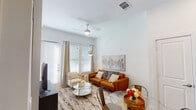 This well-appointed single-floor residence offers a thoughtfully designed open-concept layout that seamlessly connects the kitchen, dining, and living areas. The living room is bathed in natural light streaming through large windows and a glass door, dressed with blinds and floor-length curtains. A ceiling fan overhead, a warm cognac leather sofa, and a glass-top coffee table anchor the space atop a textured area rug, creating an inviting atmosphere.

The kitchen is outfitted with gray shaker-style cabinetry, granite countertops, a subway tile backsplash, and a full suite of stainless steel appliances, including a refrigerator, range, microwave, and dishwasher. A central island with bar seating provides additional prep space and casual dining. Light wood-tone flooring throughout the kitchen and dining area enhances the airy, modern feel.

Two bedrooms each feature neutral tones, carpeted floors, and windows with exterior views. The primary bedroom connects directly to a well-sized en suite bathroom, which includes a double-sink granite vanity with gray cabinetry, a soaking tub, a separate shower, and direct access to a walk-in closet. The overall ambiance is clean, contemporary, and bright throughout.