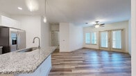 Located at 171 Town Park Dr in Conroe, TX, this well-appointed 2-bedroom, 2-bathroom residence offers a thoughtfully designed single-floor layout. The open-concept living, dining, and kitchen area forms the heart of the home, featuring wood-look flooring, a ceiling fan, and French doors that flood the space with natural light and lead out to a private balcony. The kitchen is a standout, showcasing granite countertops, two-tone cabinetry with white upper and gray lower cabinets, a hexagonal tile backsplash, stainless steel appliances, and a pantry for added storage. Pendant lighting over the kitchen island adds a stylish finishing touch. The primary bedroom is carpeted for comfort and includes direct access to its own bathroom and a dedicated closet. Both bathrooms are finished consistently with wood-look tile flooring, granite vanity countertops, dark-stained cabinetry, and full tub-shower combinations with large-format tile surrounds and brushed nickel fixtures. Additional highlights include three closets throughout the unit, a dedicated laundry area, and a dining space that flows seamlessly from the kitchen. The overall aesthetic is clean, modern, and neutral, creating a bright and inviting atmosphere throughout.