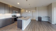 Located on Republic Drive in Colorado Springs, CO, this single-floor residence showcases a contemporary design with high-quality finishes throughout. The open-concept living and kitchen area serves as the heart of the home, featuring durable wood-look plank flooring that extends seamlessly across the space. The kitchen is equipped with dark espresso cabinetry, granite countertops, a white subway tile backsplash, and a full suite of stainless steel appliances, including a French door refrigerator, range, and microwave. A large central island with an integrated sink and pendant lighting above provides both workspace and casual dining options. The living area is filled with natural light from multiple large windows framing panoramic views of the surrounding Colorado landscape and distant mountain ranges, with a glass-panel entry door reinforcing the connection to the outdoors. The bedrooms are carpeted for comfort, each equipped with ceiling fans and generous windows capturing the same scenic views. The bathrooms feature consistent granite countertops, dark cabinetry with brushed hardware, and wood-look flooring. The primary bath includes a dual-sink vanity, built-in shelving, and a tub-shower combination with white tile surround, presenting a clean, modern aesthetic throughout.