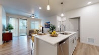 This well-appointed single-floor residence offers a thoughtfully designed layout that seamlessly blends comfort and modern style throughout. The open-concept kitchen serves as the heart of the home, showcasing a large center island with striking white quartz countertops, an undermount sink, stainless steel dishwasher, and stylish pendant lighting overhead. The kitchen flows directly into a bright, welcoming living area finished with warm wood-look flooring, a ceiling fan, and a sliding glass door that opens to an outdoor patio, filling the space with natural light.

The living room is a relaxed yet refined retreat, featuring additional windows with horizontal blinds for privacy and light control. Two well-sized bedrooms offer plush carpeting and ample natural light, with one room providing access to a generously sized walk-in closet outfitted with multiple shelving levels and hanging rods for comprehensive storage.

Both bathrooms are finished with white shaker-style cabinetry, quartz countertops, and wood-look flooring. The primary bathroom includes a walk-in glass shower, while the secondary bathroom features a full tub-shower combo. A dedicated laundry room houses a full-size top-load washer and dryer alongside open shelving, adding everyday convenience to this well-rounded home.