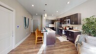 This single-floor residence is thoughtfully designed with an open-concept layout that seamlessly connects the kitchen, dining, and living areas. The kitchen is a standout feature, equipped with dark cabinetry, stainless steel appliances including a refrigerator, microwave, and range, and a generous island with a light countertop that doubles as a breakfast bar with woven bar stools. Pendant lighting illuminates the island, while recessed lighting and a textured ceiling add character overhead. Wood-look flooring runs throughout the main living areas, contributing to a cohesive and modern aesthetic.

The living room is bright and welcoming, benefiting from natural light streaming through large windows with views of the surrounding area. Neutral, warm-toned walls create a calm ambiance throughout the unit.

The bedrooms are carpeted for comfort, each featuring wide windows that invite abundant natural light. The bathroom is well-appointed with dark cabinetry, a white countertop vanity, and wood-look flooring.

A dedicated laundry area with a stacked washer and dryer unit and built-in shelving provides added convenience and practical storage, completing this well-designed space.