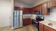 Located at 5721 Goodstone Dr in Raleigh, NC, this single-floor residence offers a well-designed layout that balances comfort and functionality. The kitchen stands out as a highlight of the home, showcasing rich cherry-toned cabinetry, light granite countertops, and a classic white subway tile backsplash. A full suite of stainless steel appliances — including a refrigerator, electric range, over-the-range microwave, and dishwasher — completes the space, making it both stylish and practical. Wood-look flooring runs through the kitchen and connecting areas, lending warmth and cohesion to the interior. The bedroom features plush wall-to-wall carpeting, neutral-toned walls, a ceiling fan with light fixture, and a bright window fitted with horizontal blinds, allowing ample natural light to fill the room. The bathroom continues the home's consistent design language with matching cabinetry, a single-sink vanity, and wood-look flooring. A walk-in closet is conveniently accessible directly from the bathroom, providing generous storage. The overall ambiance of the home is clean, modern, and move-in ready, with a neutral color palette that creates a versatile backdrop throughout every room.