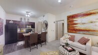 This one-bedroom, one-bathroom unit in Oklahoma City, Oklahoma, offers a practical and well-designed single-floor layout. The open-concept living and kitchen area forms the heart of the space, where rich dark wood cabinetry, granite-style countertops, and black appliances — including a refrigerator, range, and built-in microwave — define the kitchen. A breakfast bar with seating for two connects the kitchen to the living area, creating a seamless flow ideal for dining and entertaining. The carpeted living room receives natural light through large windows fitted with blinds, and is served by a ceiling fan overhead. A private entrance door opens directly into this space. The bedroom offers a comfortable, carpeted retreat with natural light from a window and ample storage via a walk-in closet with built-in shelving. The bathroom features a tub-shower combination with a sliding glass enclosure, complemented by dark wood cabinetry. A dedicated in-unit laundry area with a top-load washer and wire shelving adds everyday convenience. Throughout the unit, neutral wall tones and light-colored carpet create a clean, cohesive aesthetic.