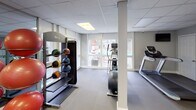 Located at 1313 Stone Mill Way in Stone Mountain, Georgia, this fitness center offers a comprehensive workout environment designed to accommodate a wide range of exercise routines. The space features a drop-panel ceiling with recessed fluorescent lighting that ensures consistent, even illumination throughout. Neutral gray walls and durable flooring — a combination of sealed concrete and interlocking rubber mat sections — create a clean, functional aesthetic.

The main workout area is generously proportioned, with structural columns integrated seamlessly into the layout. A row of large windows along one wall floods the space with natural light and provides views of the outdoor surroundings, including what appears to be a pool area and patio. A glass-paneled exterior door offers direct access to the outdoor space.

Equipment is well-organized and diverse. A full rack of dumbbells lines one wall, accompanied by a weight bench and large floor mirrors that enhance the sense of space. Medicine balls and stability balls are neatly stored on dedicated racks. Cardio equipment includes treadmills, an elliptical, a stair climber, and a rowing machine. A multi-function cable machine rounds out the strength training offerings.

A separate storage or utility area with closet doors is accessible from the main floor, along with a staircase providing access to an upper level.