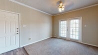 This single-floor residence offers a thoughtfully designed layout with a consistent warm, neutral color palette throughout. The living area is highlighted by plush carpeting, elegant crown molding, a ceiling fan with integrated lighting, and a set of French doors fitted with blinds that invite natural light and provide access to the outdoors. The flooring transitions seamlessly from carpet to durable hardwood-style vinyl in the adjoining spaces, creating a cohesive visual flow. A dedicated dining or flex room features chair-rail molding, recessed lighting, and the same hardwood-style flooring, lending a refined, functional character to the space. The galley-style kitchen is well-equipped with light wood cabinetry, dark granite-style countertops, a full suite of black and stainless steel appliances, a built-in sink, and a door leading to an additional utility or pantry area. The bedrooms are finished with soft carpeting and clean white walls, offering comfortable, versatile spaces. The bathrooms feature hardwood-style flooring, warm wood cabinetry, tile-surround soaking tubs, and ample vanity storage. A spacious walk-in closet with wire shelving provides generous storage capacity. Crown molding and consistent finishes throughout the space contribute to a polished, cohesive aesthetic.