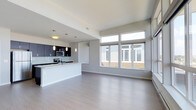 This 2-bedroom, 2-bathroom residence showcases a thoughtfully designed open-concept floor plan that seamlessly connects the kitchen and living areas into one cohesive, light-filled space. The interior is finished with smooth light-toned hardwood-style flooring that runs throughout, complementing the neutral gray and white color palette that gives the space a clean, contemporary aesthetic.

The kitchen is outfitted with dark espresso cabinetry contrasted against light countertops, creating a striking visual balance. A subway tile backsplash adds texture, while stainless steel appliances provide a polished, modern touch. Pendant lighting hangs above the kitchen peninsula, which doubles as a breakfast bar and provides additional prep space. Recessed and pendant fixtures offer layered lighting throughout.

The living area benefits from an impressive bank of oversized windows that draw in generous amounts of natural light and offer outward views to the surroundings. The elevated window placement ensures both brightness and privacy. Elevated ceilings further enhance the sense of openness and volume in the main living space. The overall ambiance is modern, airy, and functional, designed for comfortable everyday living.