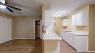 This single-floor unit is thoughtfully laid out to maximize functionality across its living spaces. The kitchen serves as a central hub, outfitted with white cabinetry, a light-toned countertop peninsula that doubles as a breakfast bar, an electric cooktop, a double sink, and a refrigerator. Track lighting illuminates the workspace, while light wood-style flooring ties the kitchen seamlessly to the adjacent living area. The textured ceilings add a classic touch throughout.

The living area is open and airy, with warm golden-beige walls, light wood flooring, and a ceiling fan with an integrated light fixture. A wall-mounted air conditioning unit provides climate control, and a wide window allows natural light to fill the space. A closet is conveniently accessible from this area.

The bedrooms feature plush carpeting, warm-toned walls, and ceiling fans for comfort. Each room includes a window with blinds, providing natural light and ventilation. Closet space is available within the bedroom areas, offering practical storage solutions. White baseboards throughout the unit provide a clean, finished appearance, contributing to an overall functional and comfortable living environment.