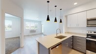 This single-floor unit showcases a contemporary design with a bright, open layout and light-toned finishes throughout. The open-concept living and kitchen area serves as the heart of the space, where light wood-style flooring flows seamlessly underfoot. The kitchen is well-appointed with two-tone cabinetry — white upper cabinets paired with charcoal lower units — and a full suite of stainless steel appliances including a refrigerator, electric range, microwave, and dishwasher. A peninsula island with a light countertop and undermount sink anchors the space, illuminated by a trio of striking black cone pendant lights. A dedicated laundry area with a side-by-side washer and dryer is conveniently situated nearby.

The bedrooms offer a calm retreat, one featuring plush carpeting and another with hardwood-style flooring, both with windows overlooking lush greenery. Each bathroom is cleanly finished with light countertops, gray or blue cabinetry, undermount sinks, and tub-shower combinations. The overall ambiance is clean, modern, and functional, with abundant natural light enhancing the fresh, neutral palette throughout.