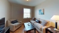 This single-floor residence offers a thoughtfully designed layout across two bedrooms and two full bathrooms. The kitchen is a functional highlight, featuring rich medium-toned wood cabinetry, dark granite countertops with a speckled finish, black appliances including a range and microwave, and a stainless steel sink. A pendant light above the extended breakfast bar adds warmth to the space, while wood-look flooring ties the area together.

The living room provides a comfortable gathering space with hardwood flooring, crown molding, and a large window that brings in natural light and views of the surrounding area. Both bedrooms are carpeted and share a similarly neutral, calming palette. Each room features windows with outdoor views, providing ample natural light. One bedroom also showcases decorative wall paneling for added architectural detail.

A dedicated workspace or study nook with large windows and plush carpet offers versatility. Both bathrooms feature light tile flooring, pedestal sinks, framed mirrors, and shower-curtain enclosures — one with a walk-in shower and the other with a tub-shower combination — maintaining a clean, consistent aesthetic throughout.