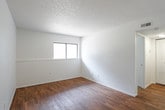 This single-floor space offers a clean, functional layout designed for comfortable everyday living. The interior is finished with crisp white walls, white trim, and textured ceilings throughout, creating a bright and cohesive aesthetic.

The living area is generously proportioned, featuring warm wood-look laminate flooring that extends through the main areas. Large windows fitted with horizontal blinds allow natural light to filter in, enhancing the open feel of the space. The layout flows naturally from the living area toward the kitchen and connecting rooms.

The galley-style kitchen is well-equipped and efficiently designed, with ample white cabinetry lining both sides of the room. Stone-patterned laminate countertops provide practical workspace, while a stainless steel sink, electric coil range, refrigerator, and dishwasher complete the suite of appliances. Wood-look flooring continues underfoot, tying the kitchen seamlessly to the rest of the unit.

The bedroom is a quiet, comfortable retreat featuring plush wall-to-wall carpeting in a neutral tan tone. A window provides natural light, and the room's clean, uncluttered walls offer flexibility for a variety of furniture arrangements. A closet provides convenient storage.

Overall, the space presents a tidy, move-in-ready environment with a practical floor plan and consistent, neutral finishes throughout.